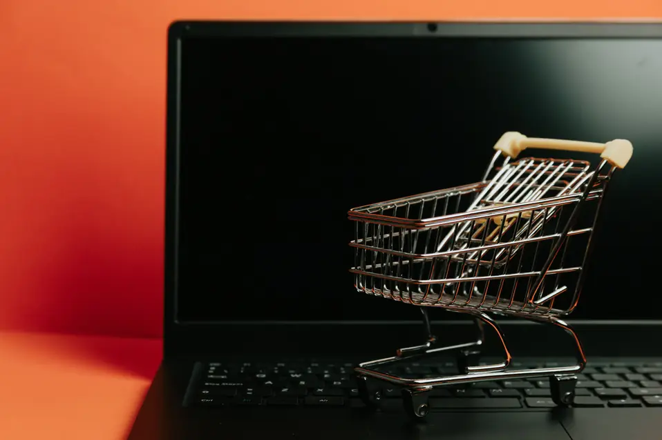 Miniature shopping cart on a laptop keyboard representing agentic commerce and Shopify catalog search